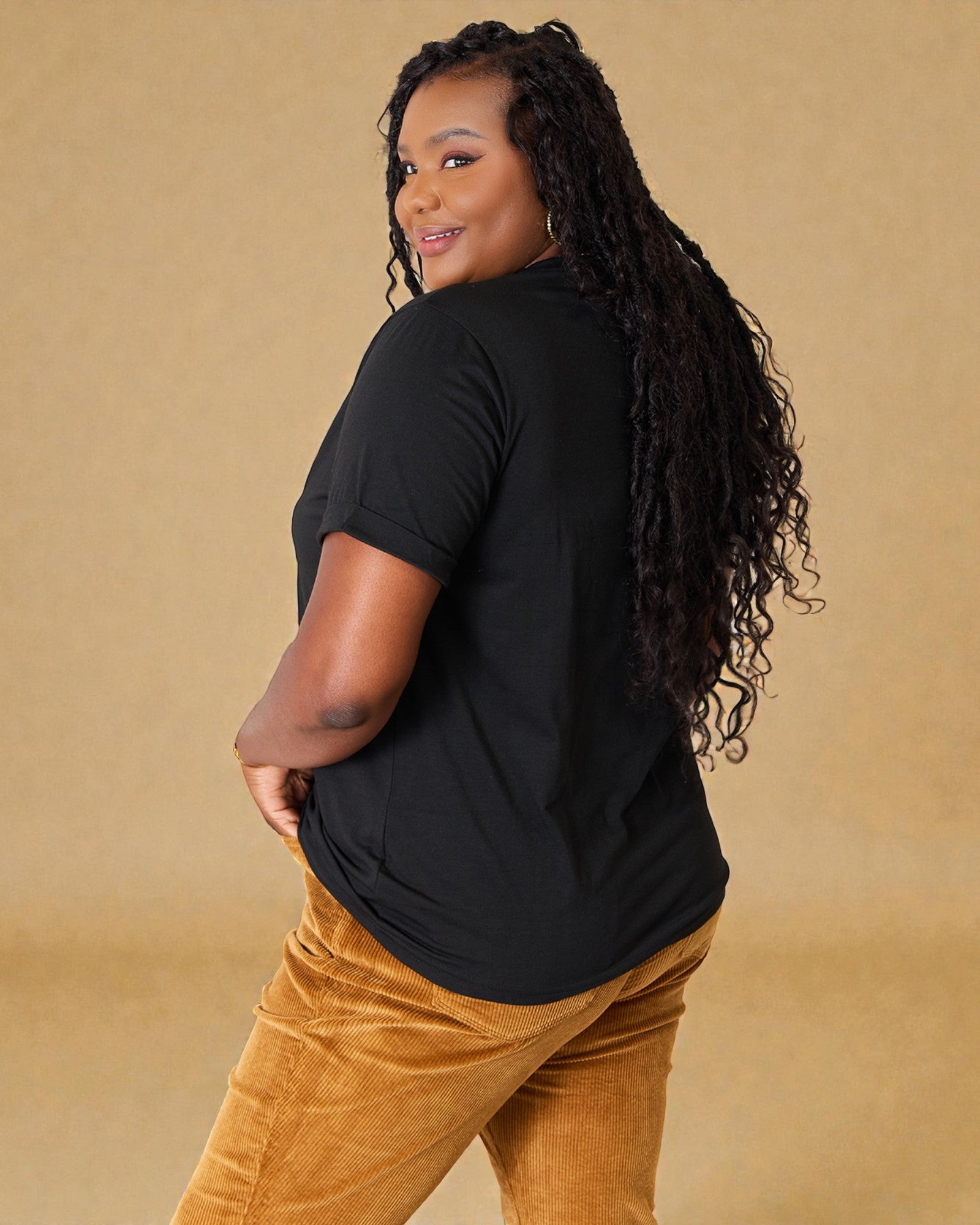 Woman wearing a black t-shirt and brown pants against a beige background