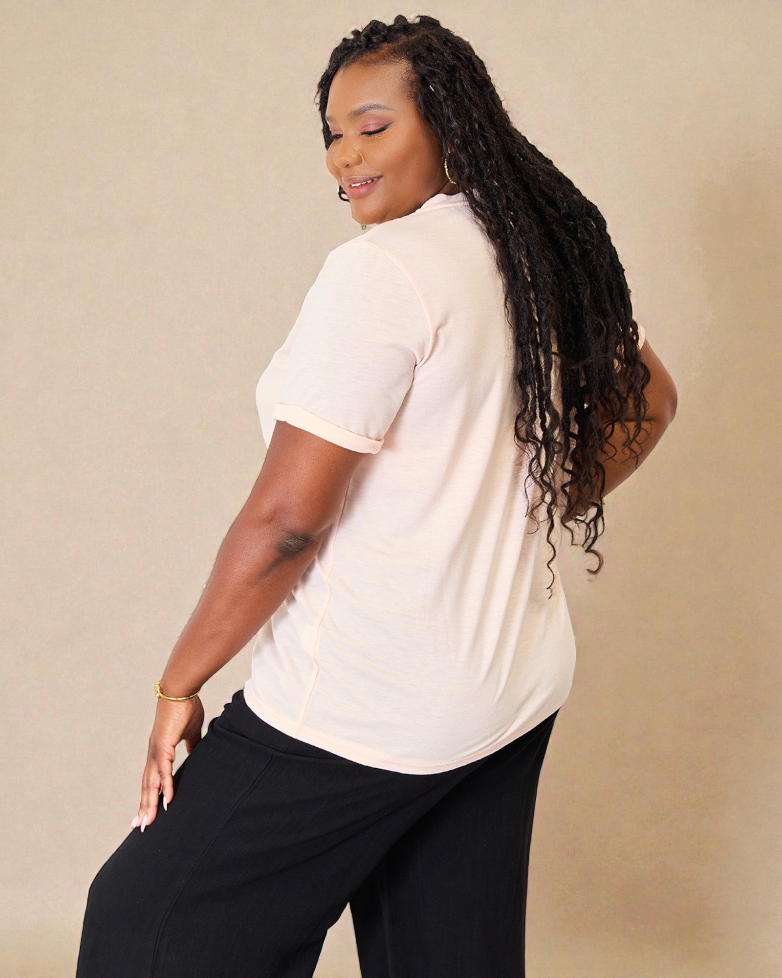 Woman wearing a beige shirt and black pants against a beige background
