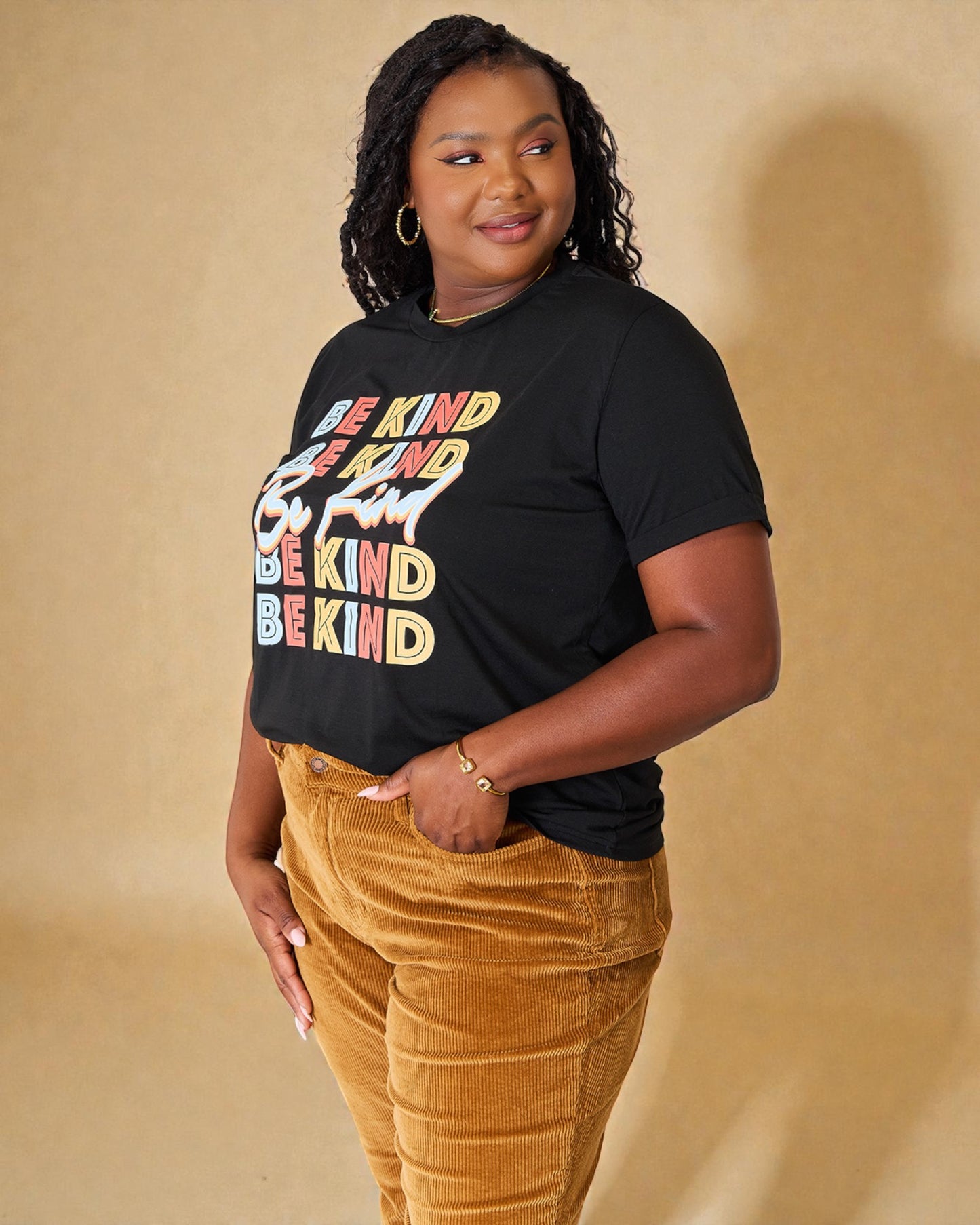 Person wearing a black t-shirt with 'Be Kind' in colorful letters on a beige background