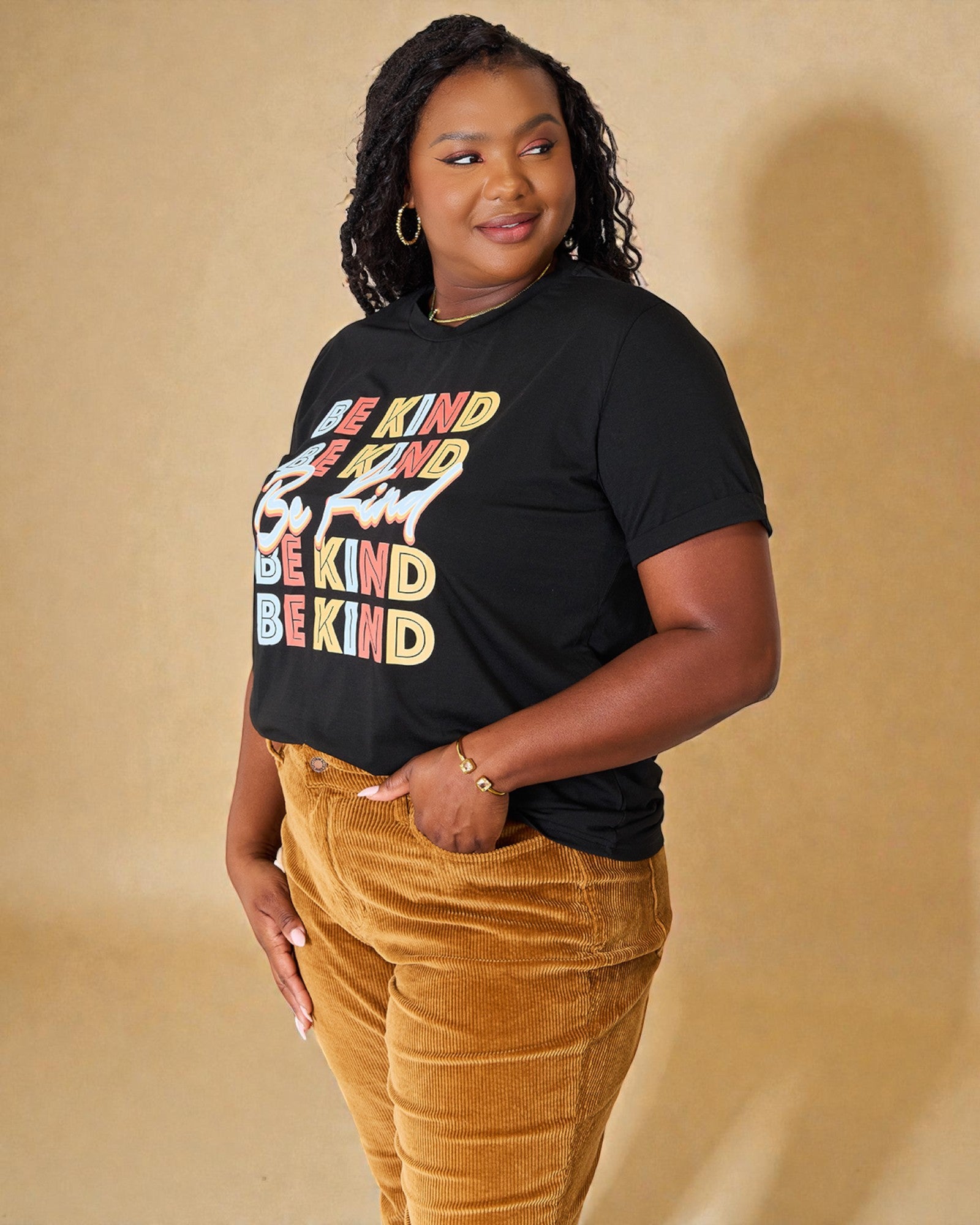 Person wearing a black t-shirt with 'Be Kind' in colorful letters on a beige background