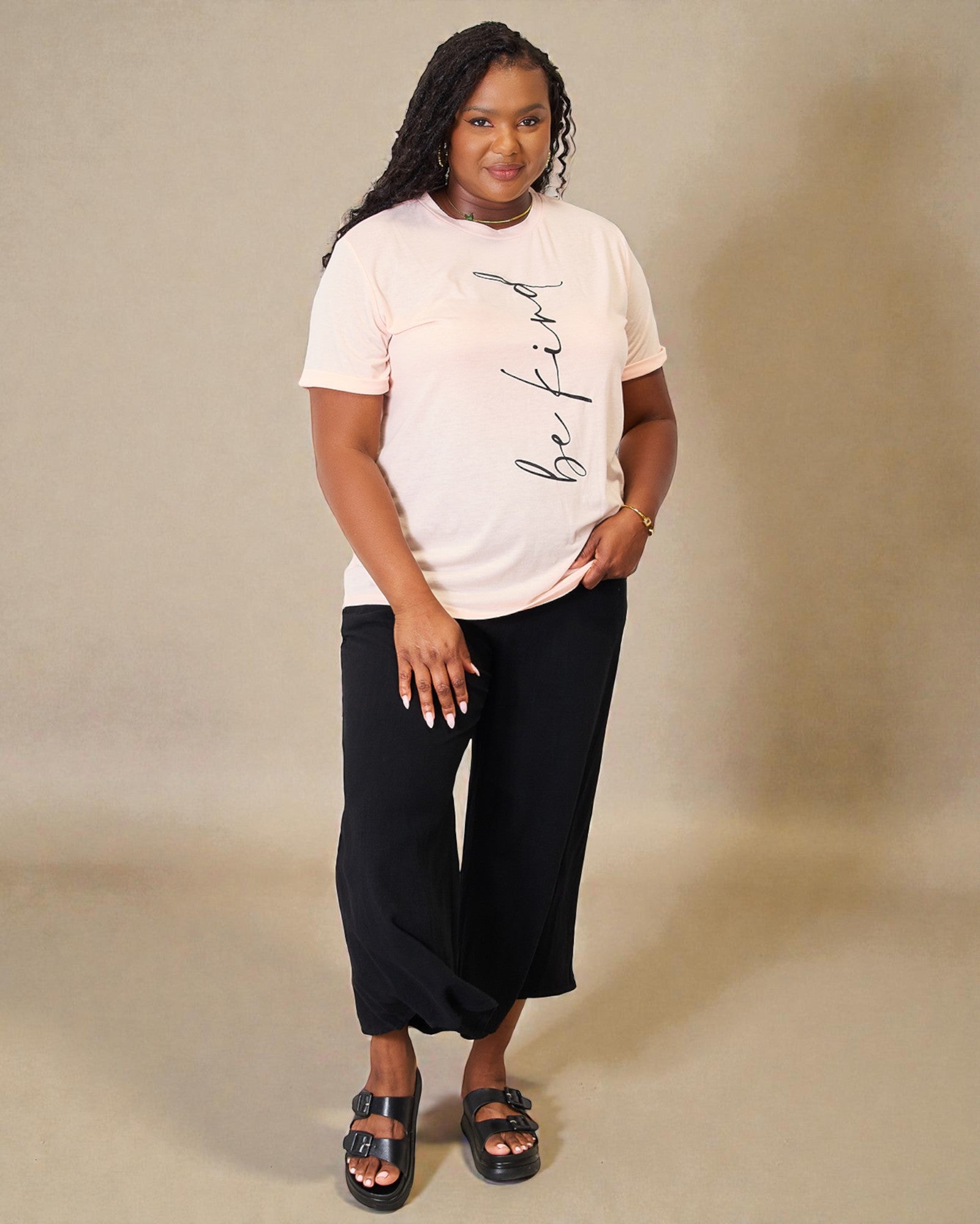 Woman wearing a white t-shirt with text and black pants on a beige background