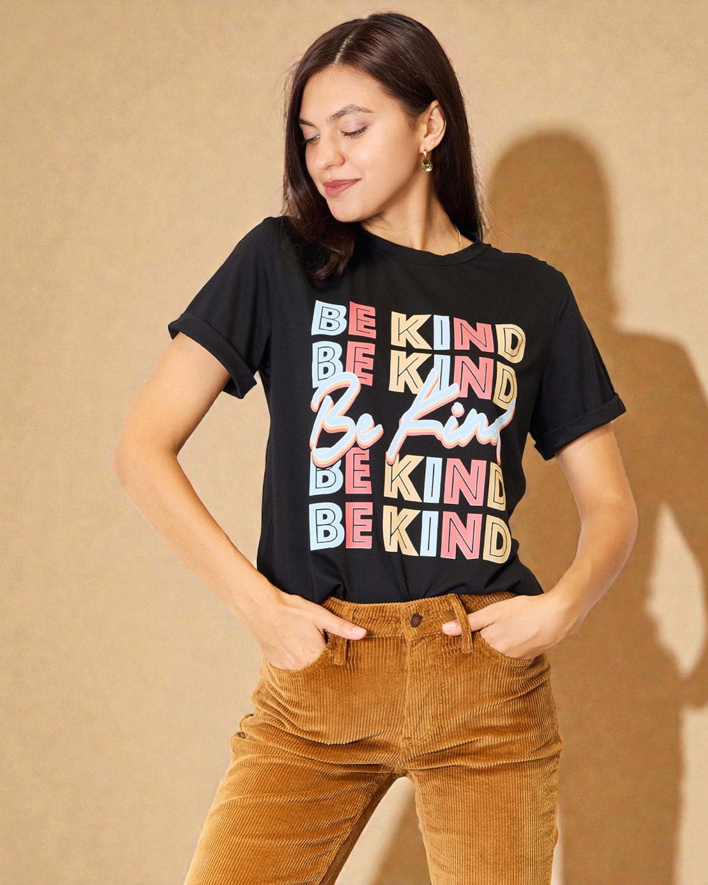 Woman wearing a black t-shirt with 'Be Kind' text in colorful letters against a beige background