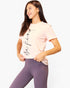 A woman wearing a light pink short-sleeve t-shirt with 'we find' printed in black script on the front, paired with purple leggings, against a plain white background.