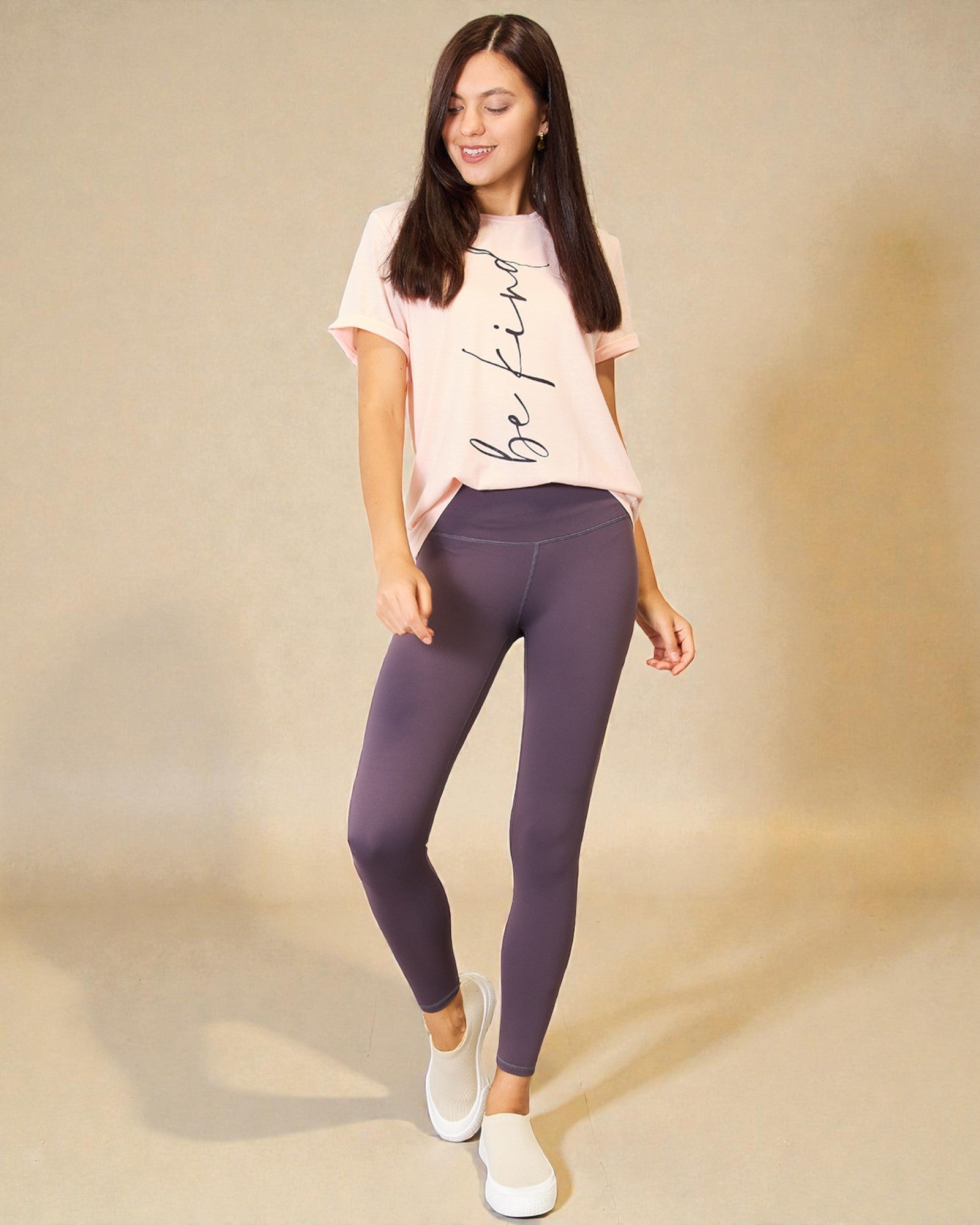 Woman wearing a pink t-shirt and purple leggings on a beige background