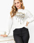 A woman wearing a white crewneck sweatshirt with a gold and black leopard print dripping lips graphic on the front, paired with black pants.