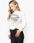 A woman wearing a white long-sleeve sweatshirt with a leopard print dripping lips graphic on the front, paired with black pants, against a plain white background.