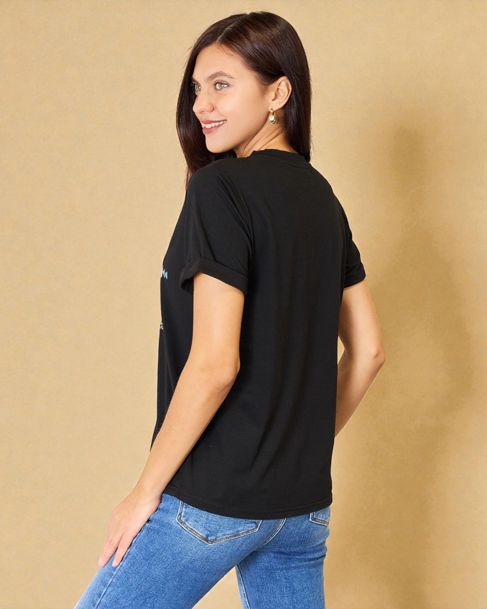 Woman wearing a black t-shirt and blue jeans against a beige background