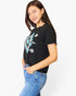 A woman wearing a black short-sleeve t-shirt with a colorful geometric tribal-style graphic on the front, paired with blue jeans, photographed against a plain white background.