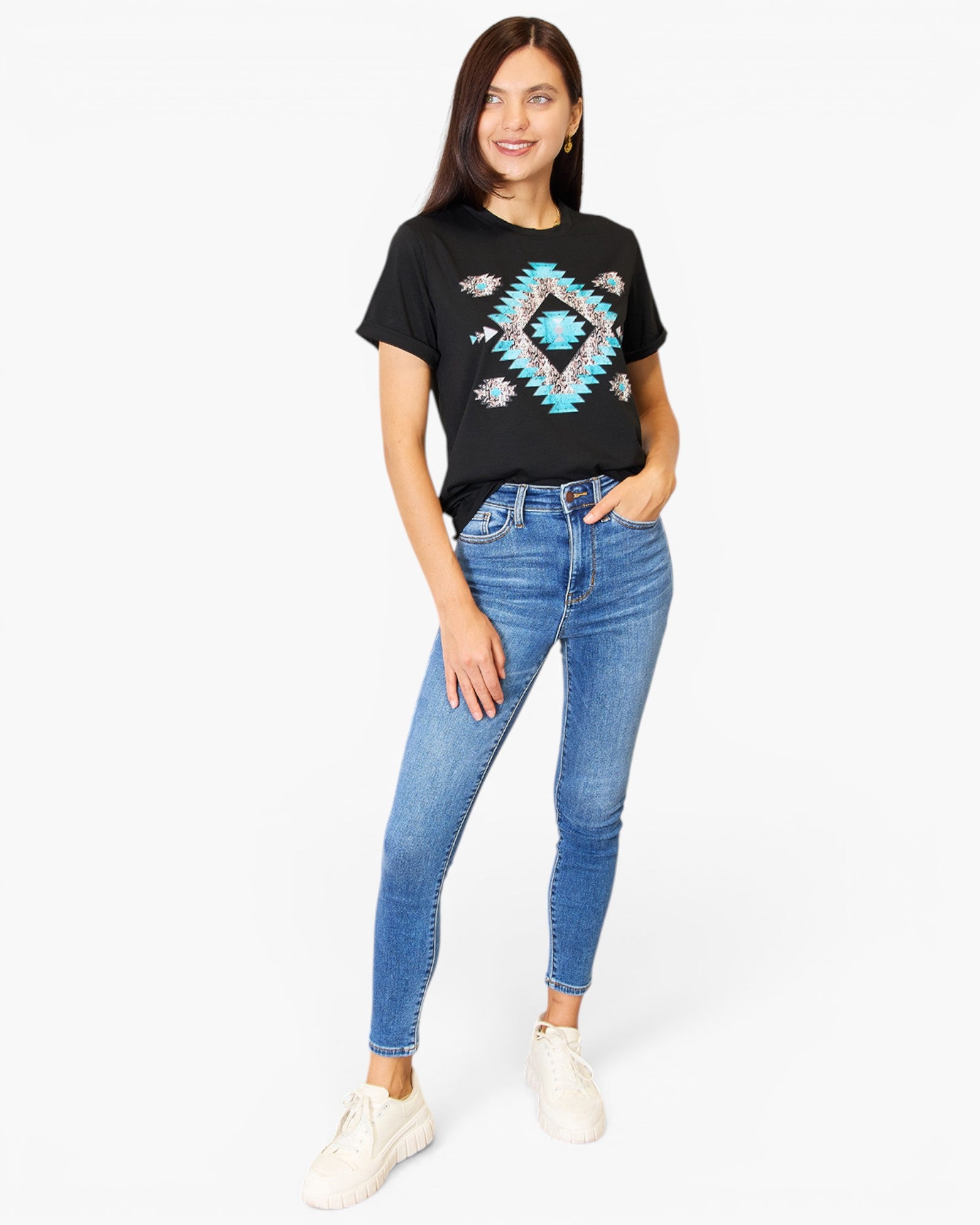 A woman modeling a black short-sleeve t-shirt with a colorful geometric diamond pattern on the front, paired with blue skinny jeans and white sneakers, against a plain white background.