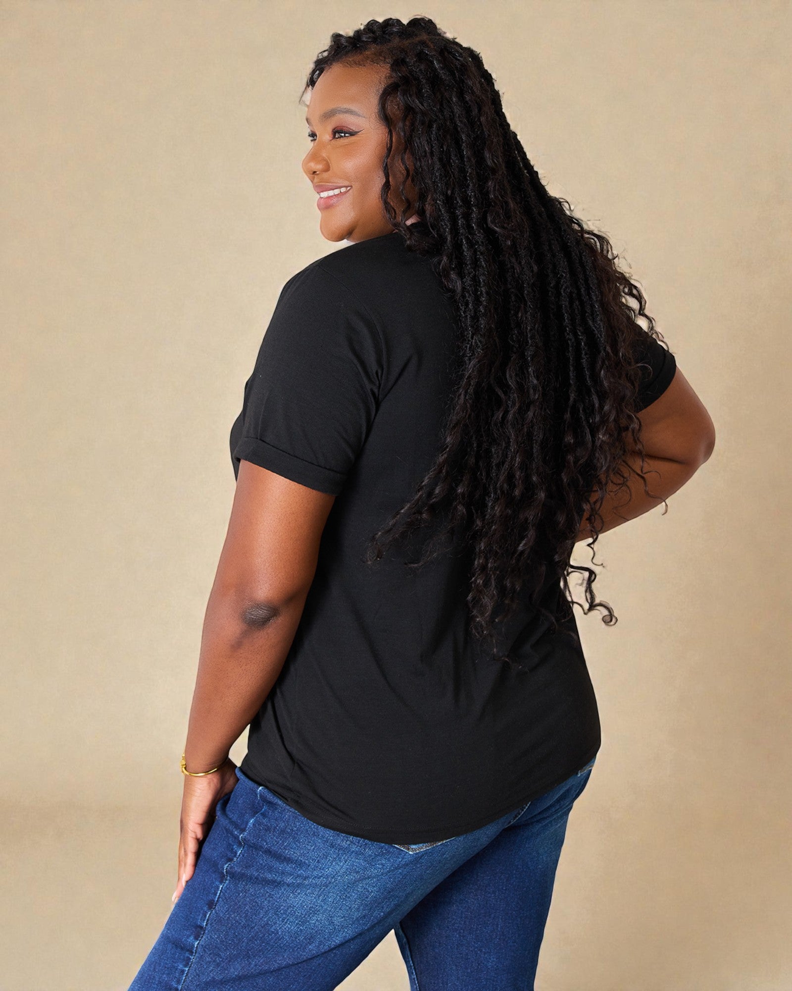 Woman wearing a black t-shirt and blue jeans against a beige background