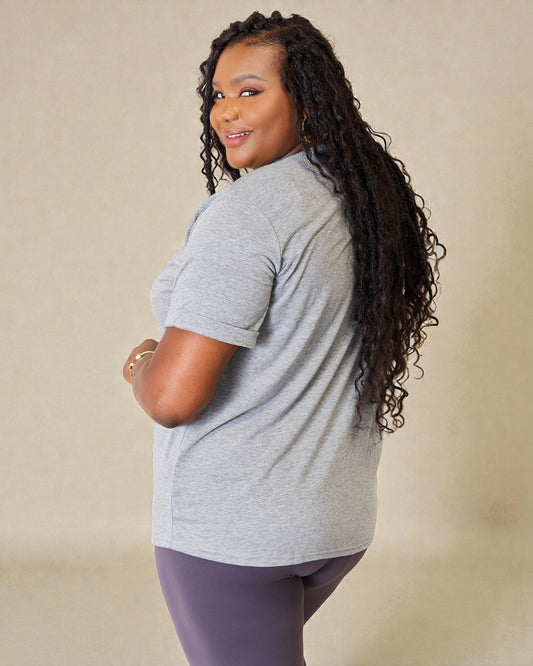 Woman wearing a gray t-shirt and purple leggings against a beige background