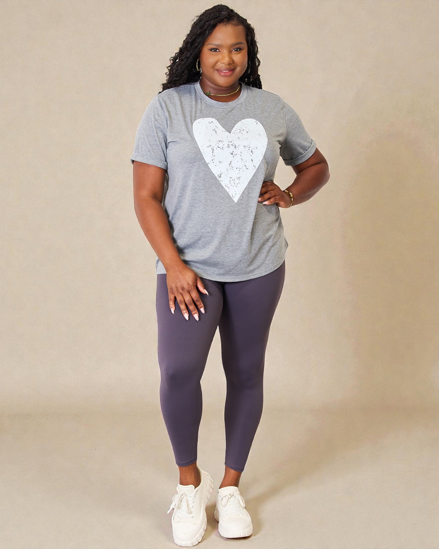 Woman wearing a gray t-shirt with a white heart design and purple leggings on a beige background