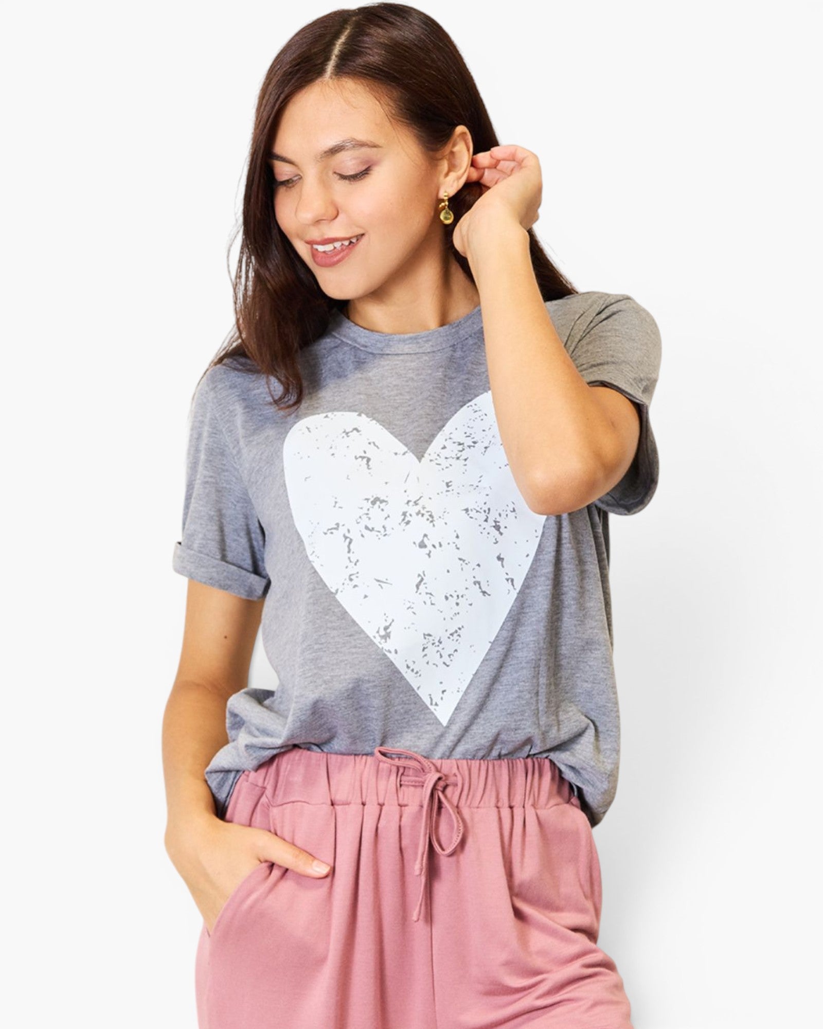 A woman wearing a heather gray t-shirt with a large white distressed heart graphic on the front, paired with dusty pink drawstring pants, against a plain white background.