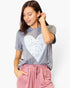 A woman wearing a heather gray t-shirt with a large white distressed heart graphic on the front, paired with dusty pink drawstring pants, against a plain white background.