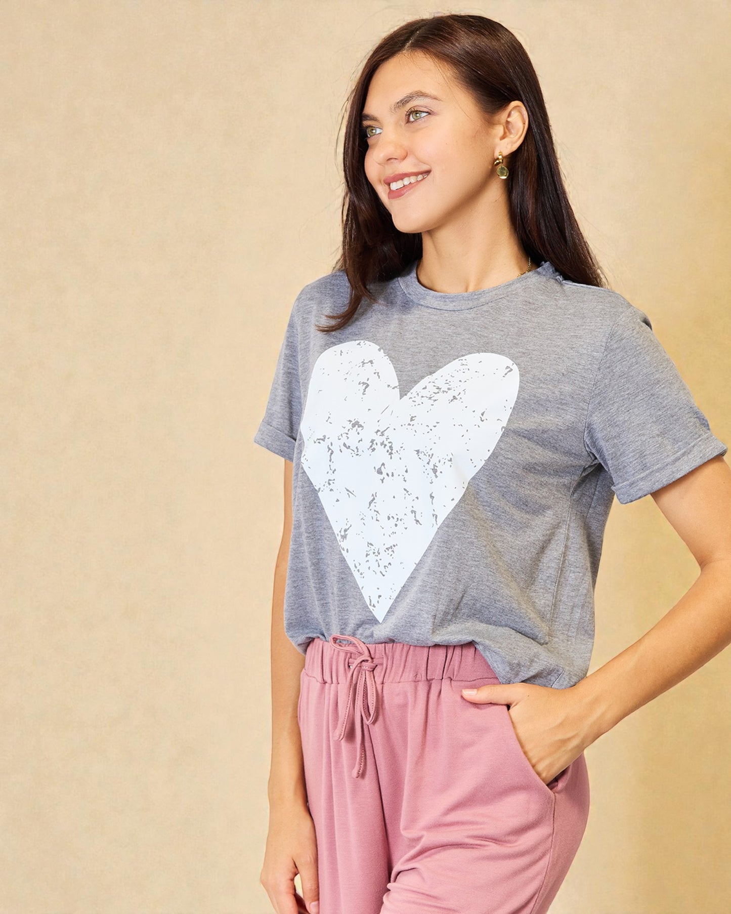 Woman wearing a gray t-shirt with a white heart design and pink pants against a beige background