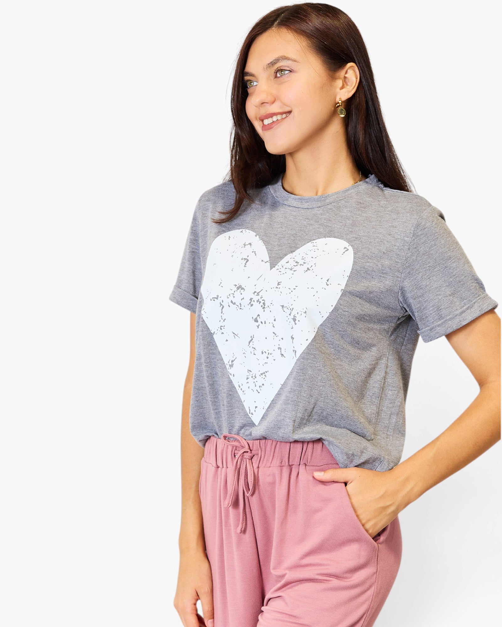 A woman wearing a heather gray short-sleeve t-shirt with a large white distressed heart graphic on the front, paired with dusty pink drawstring sweatpants, against a plain white background.