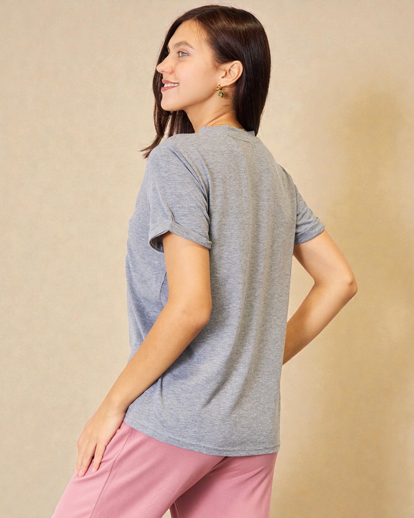 Woman wearing a gray t-shirt and pink pants against a beige background