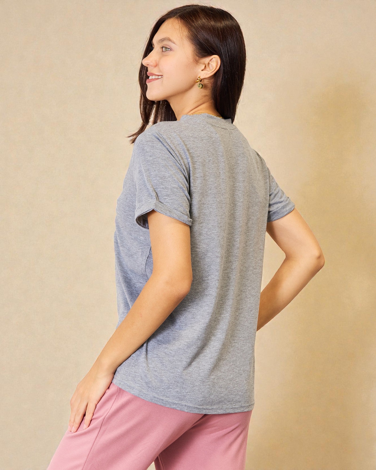 Woman wearing a gray t-shirt and pink pants against a beige background
