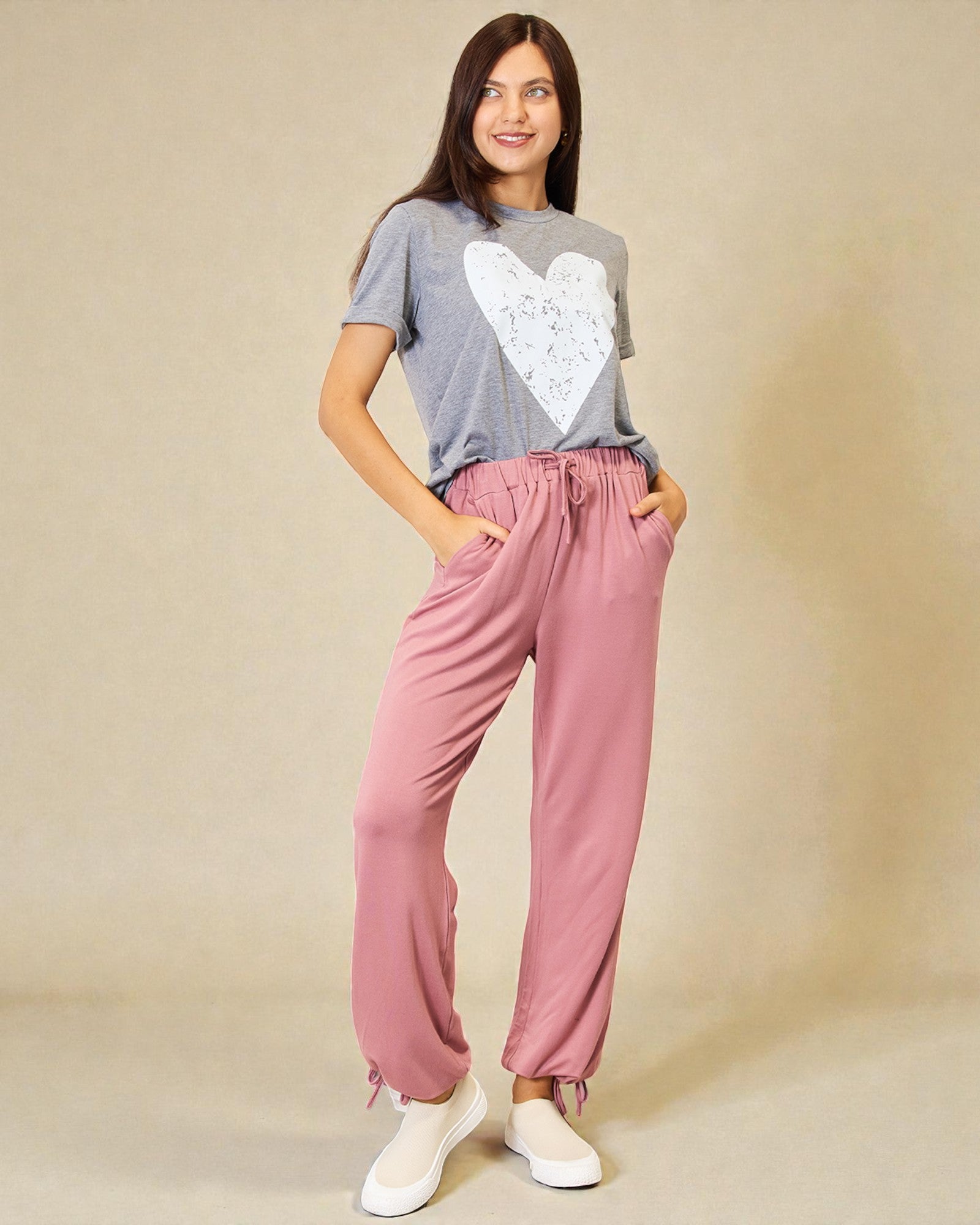 Woman wearing a gray t-shirt with a heart design and pink pants on a beige background