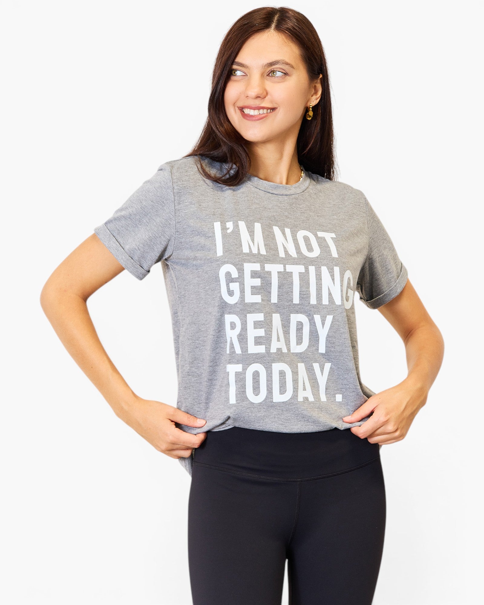 A woman wearing a heather gray graphic t-shirt with the text 'I'M NOT GETTING READY TODAY.' in white block letters, paired with black leggings, against a plain white background.