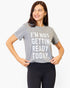 A woman wearing a heather gray graphic t-shirt with the text 'I'M NOT GETTING READY TODAY.' in white block letters, paired with black leggings, against a plain white background.