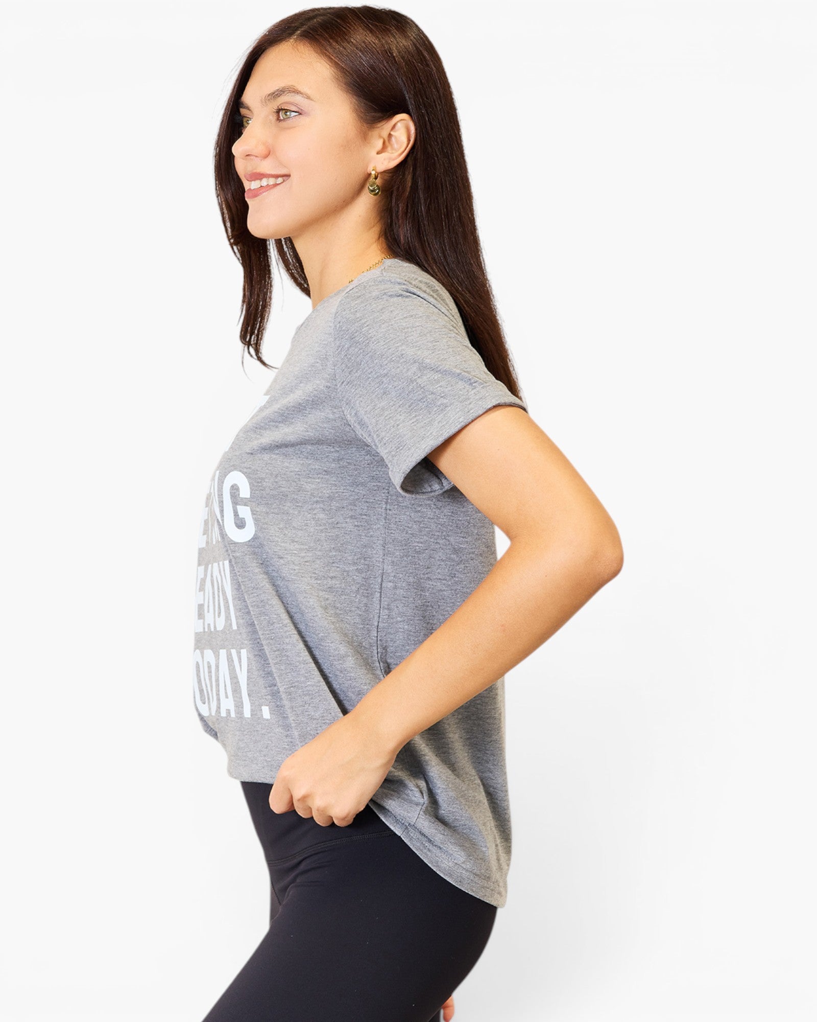 A woman wearing a heather gray short-sleeve graphic t-shirt and black leggings, shown from a side profile against a plain white studio background.