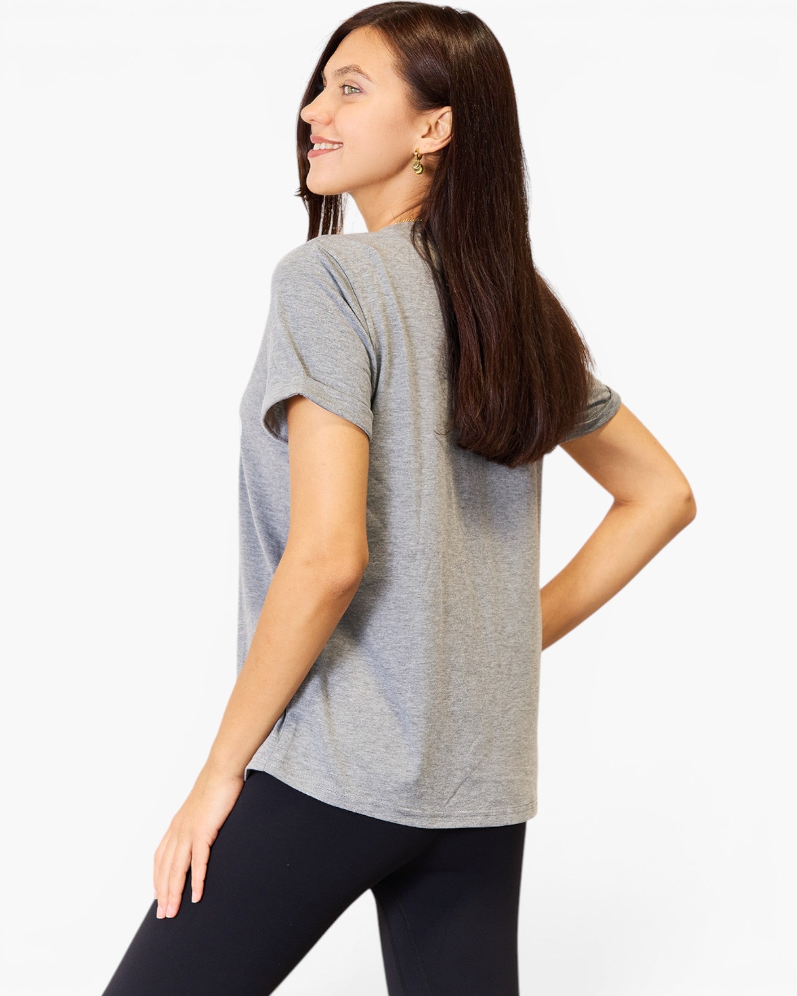 A woman wearing a heather gray short-sleeve t-shirt and black leggings, shown from a side-back angle against a plain white studio background.