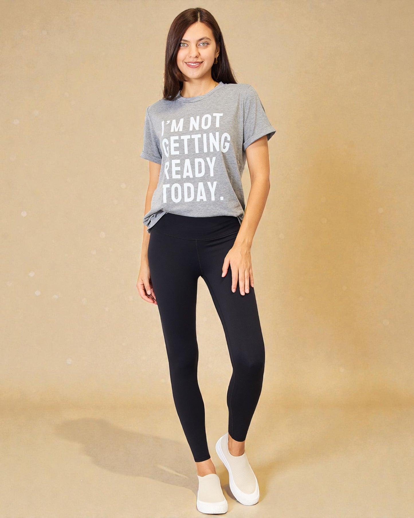 Woman wearing a gray t-shirt with text and black leggings on a beige background