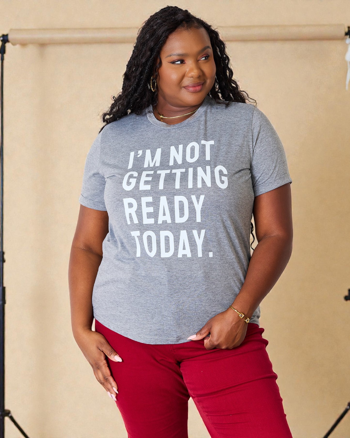 Person wearing a gray t-shirt with 'I'm not getting ready today' text, standing against a beige background.