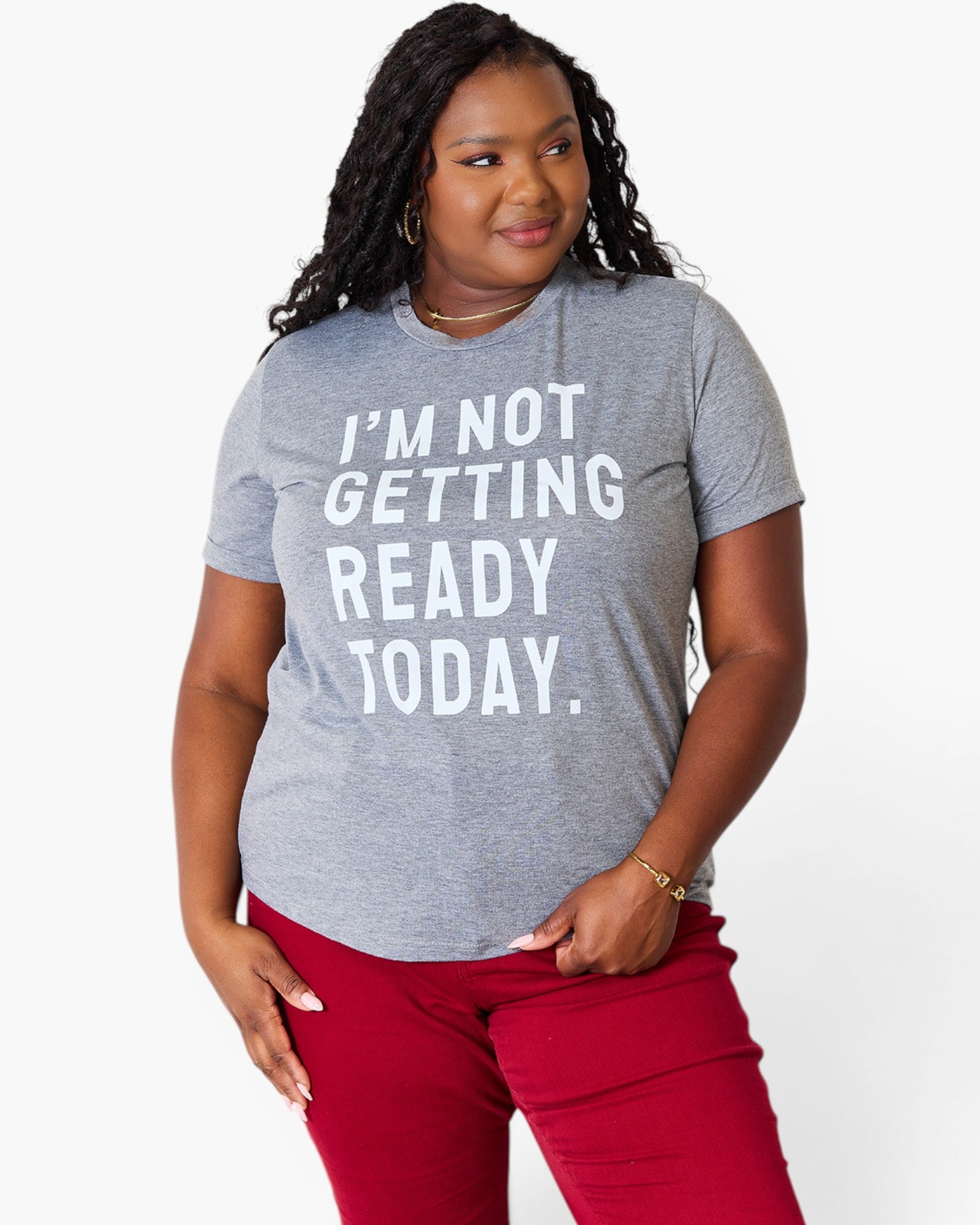 A woman wearing a heather gray graphic t-shirt with the text 'I'M NOT GETTING READY TODAY.' in bold white letters, paired with red pants, against a plain white background.