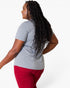 A woman with long, curly black hair is shown from a side-back angle wearing a heather gray short-sleeve t-shirt and red pants against a plain white studio background.