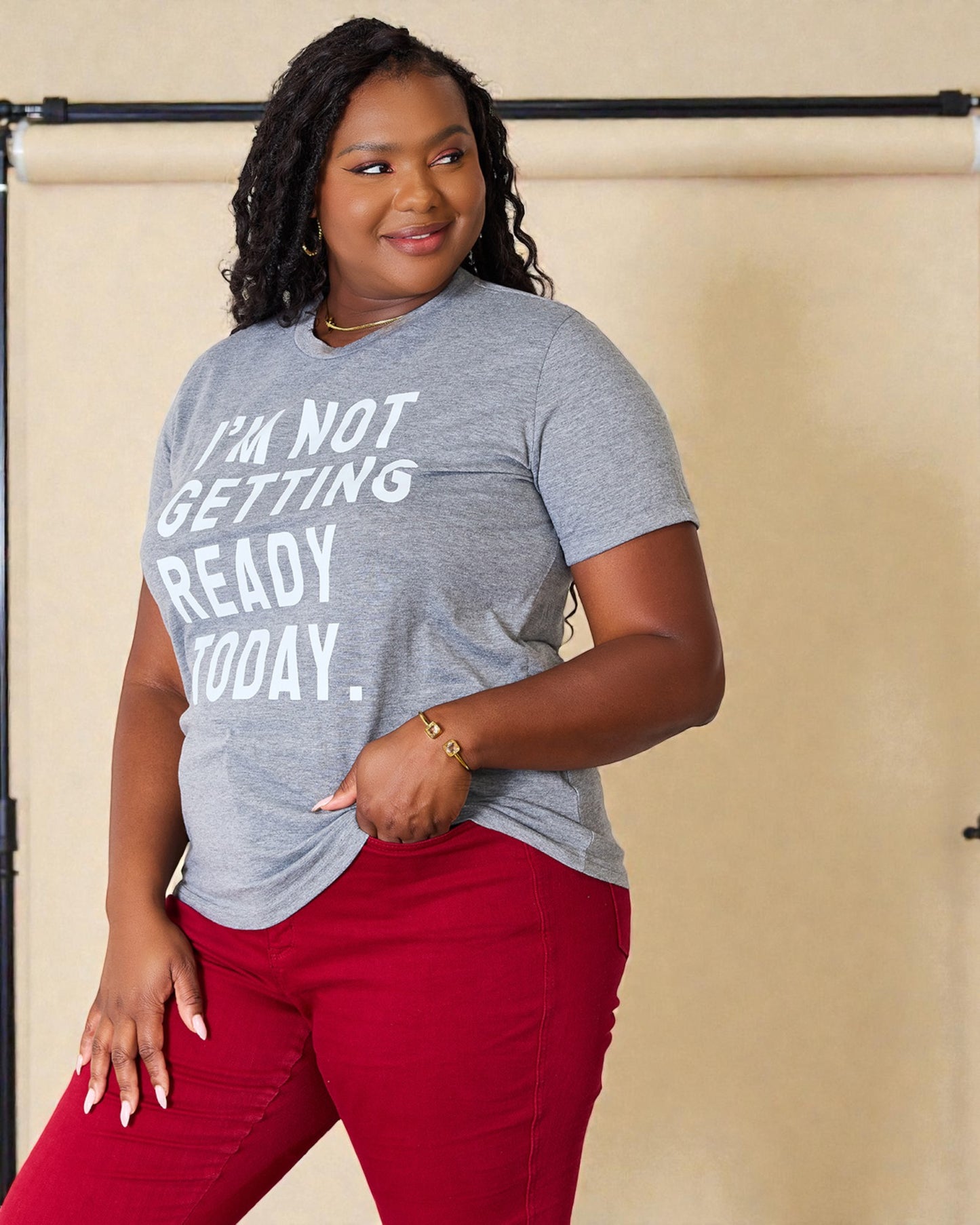 Woman wearing a gray t-shirt with text and red pants against a beige background