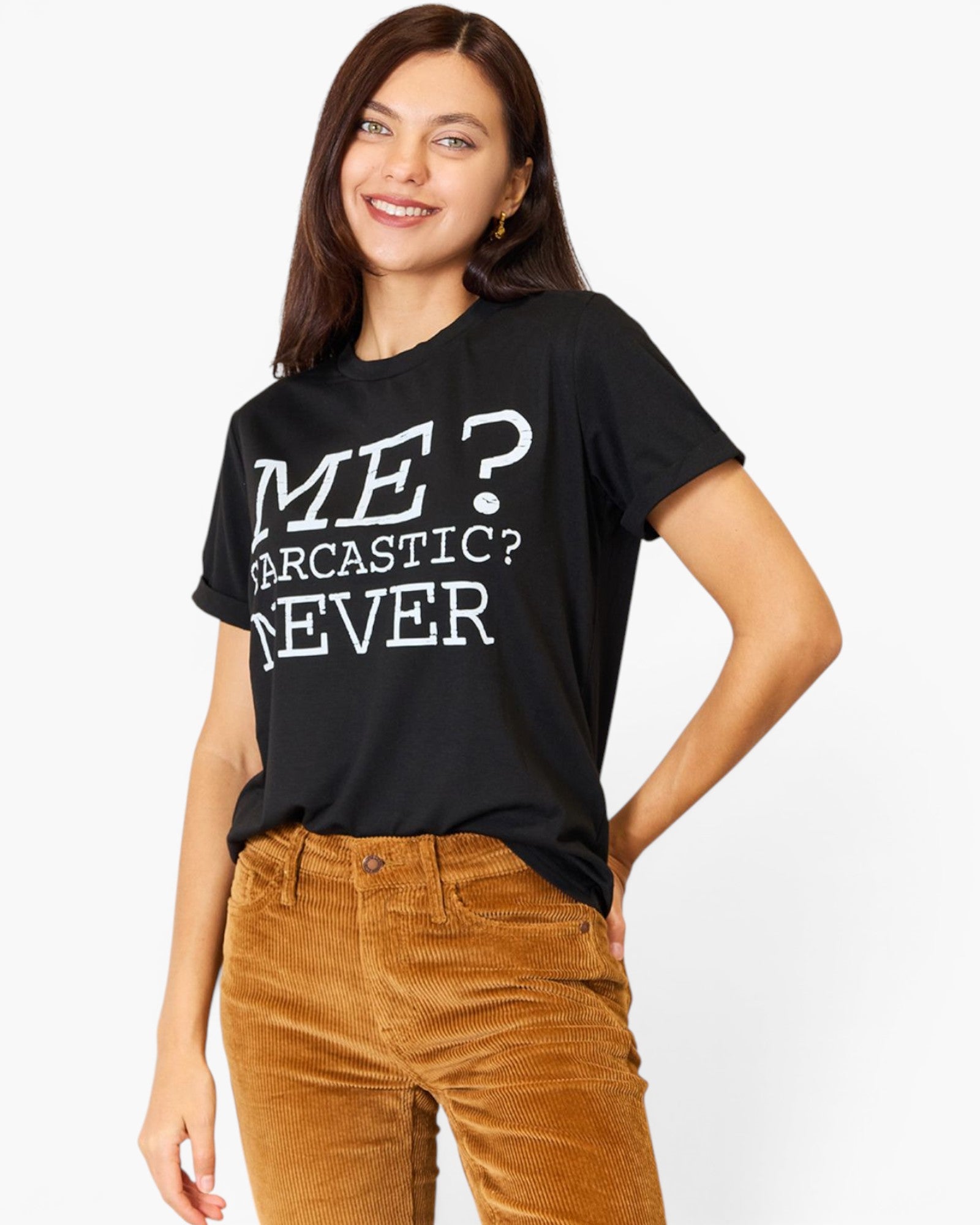 A woman wearing a black graphic t-shirt with white text that reads 'ME? SARCASTIC? NEVER' and brown corduroy pants, posing against a light gray studio background.
