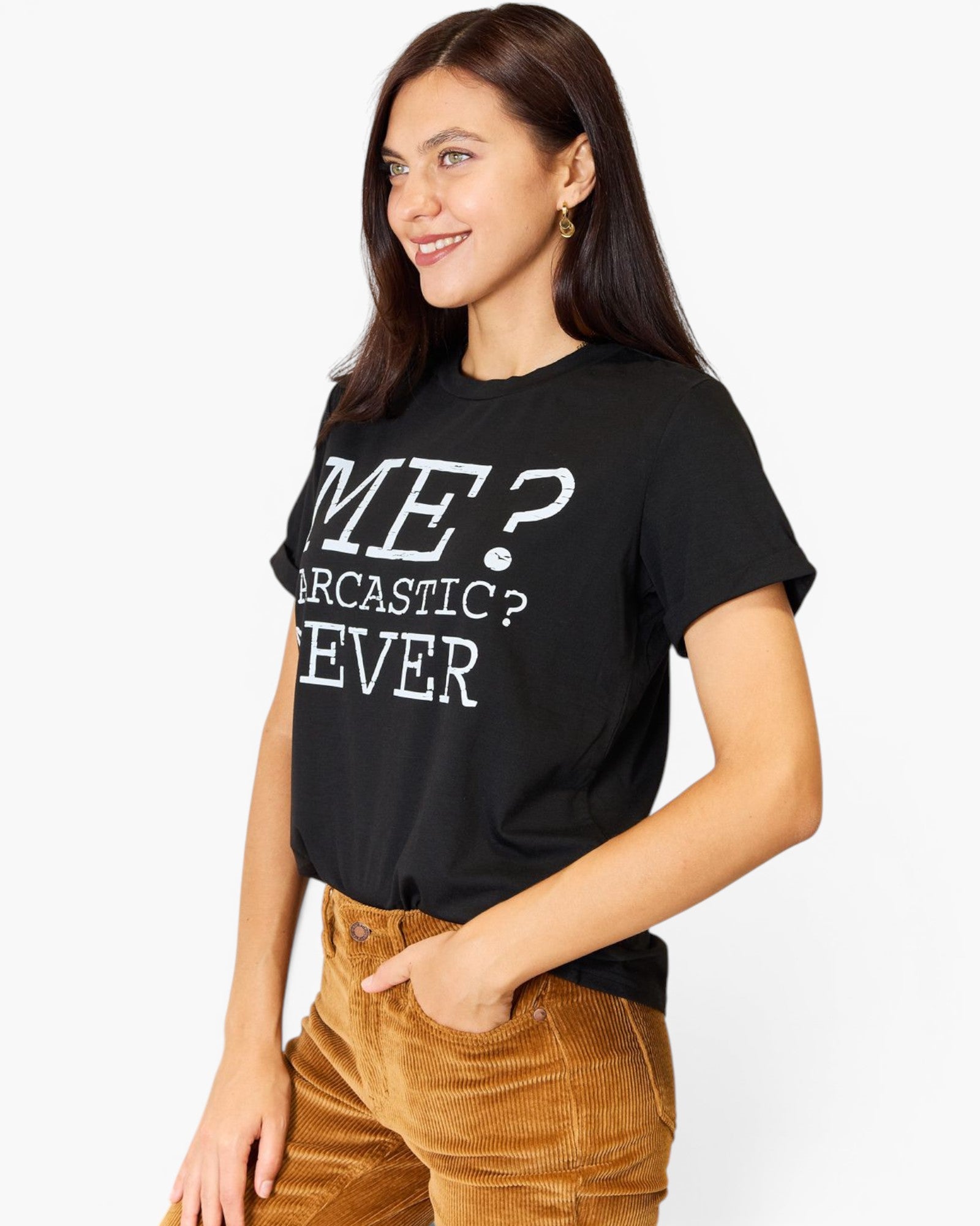 A woman wearing a black graphic t-shirt with white text that reads 'ME? SARCASTIC? NEVER' and brown corduroy pants, posing against a light gray studio background.