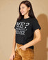 Woman wearing a black t-shirt with text, standing against a beige background