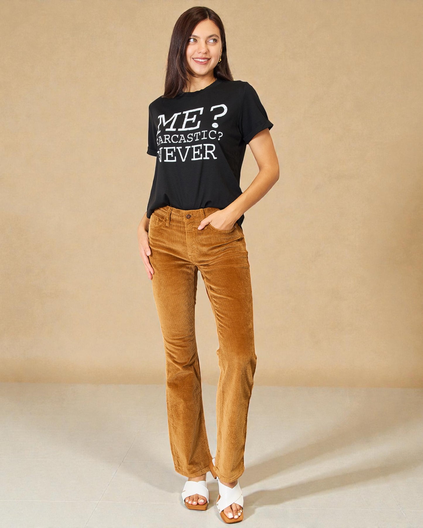 Woman wearing a black t-shirt with text and brown pants against a beige background