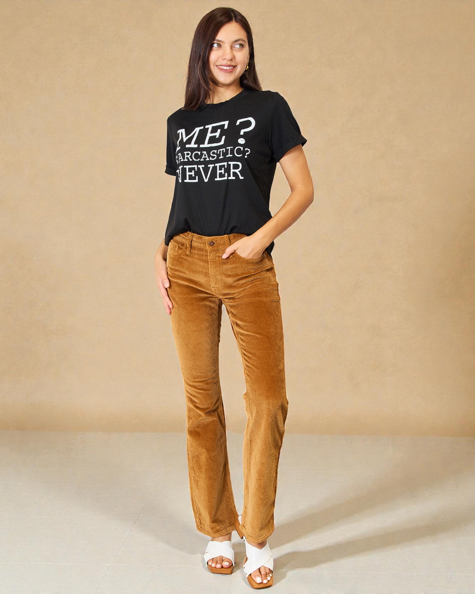 Woman wearing a black t-shirt with text and brown pants against a beige background