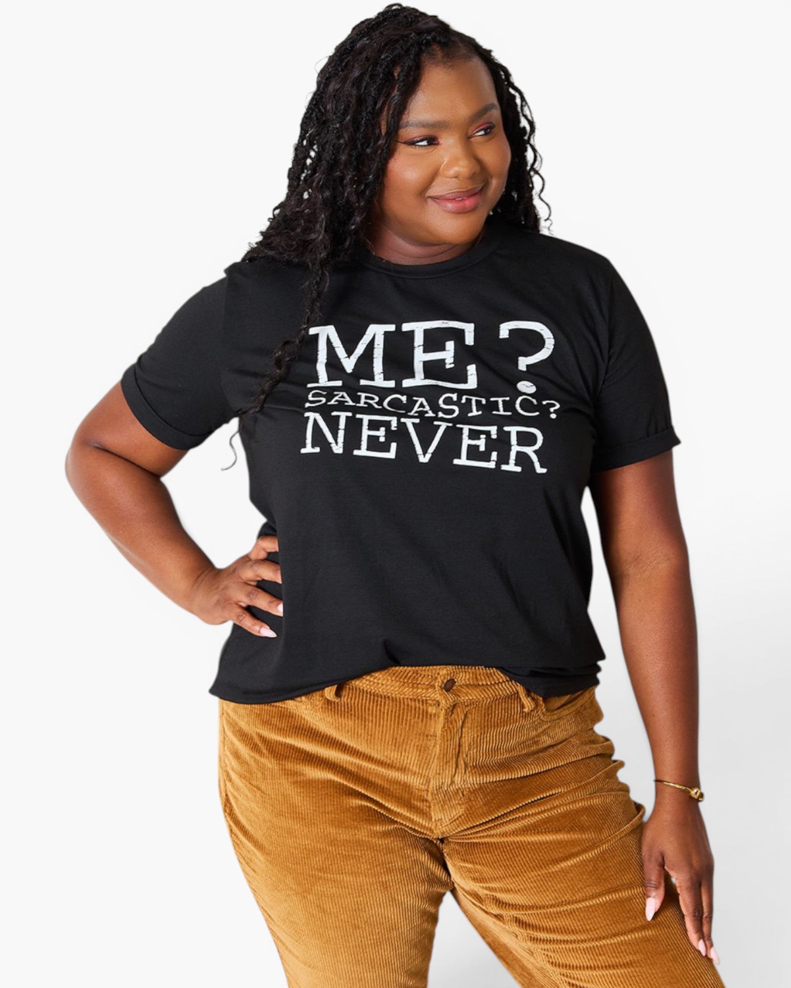 A woman modeling a black graphic t-shirt with white text that reads 'ME? SARCASTIC? NEVER'. She is wearing brown corduroy pants against a clean white background.