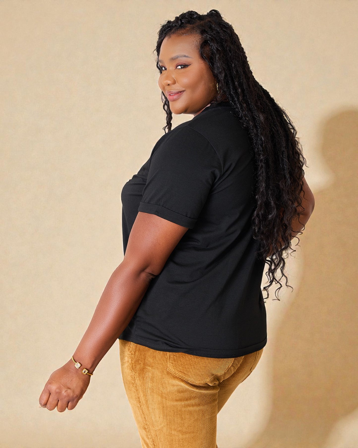 Woman wearing a black t-shirt and mustard pants against a beige background