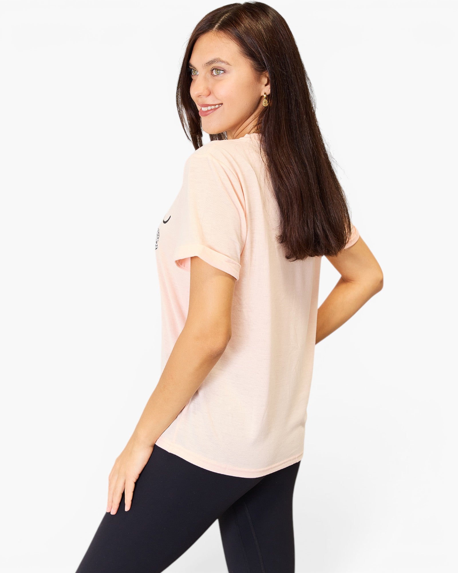 A woman modeling a light pink short-sleeve athletic t-shirt from the back, paired with black leggings, against a plain white studio background.