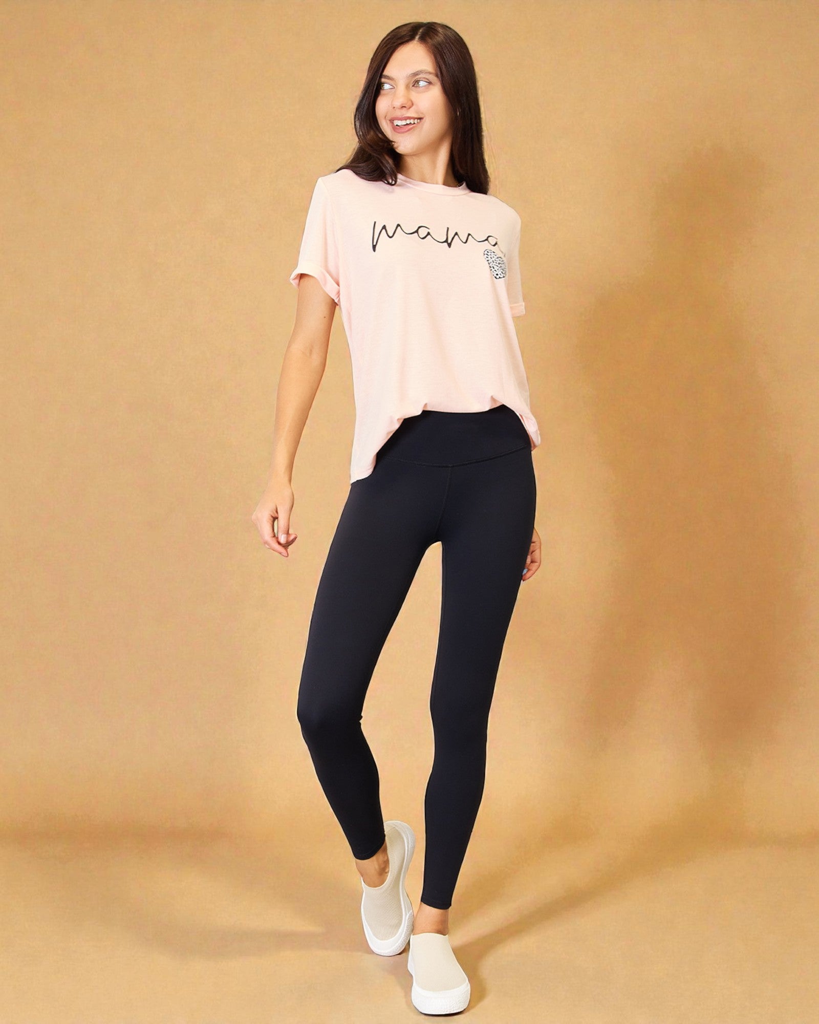 Woman wearing a light pink t-shirt and black leggings on a beige background