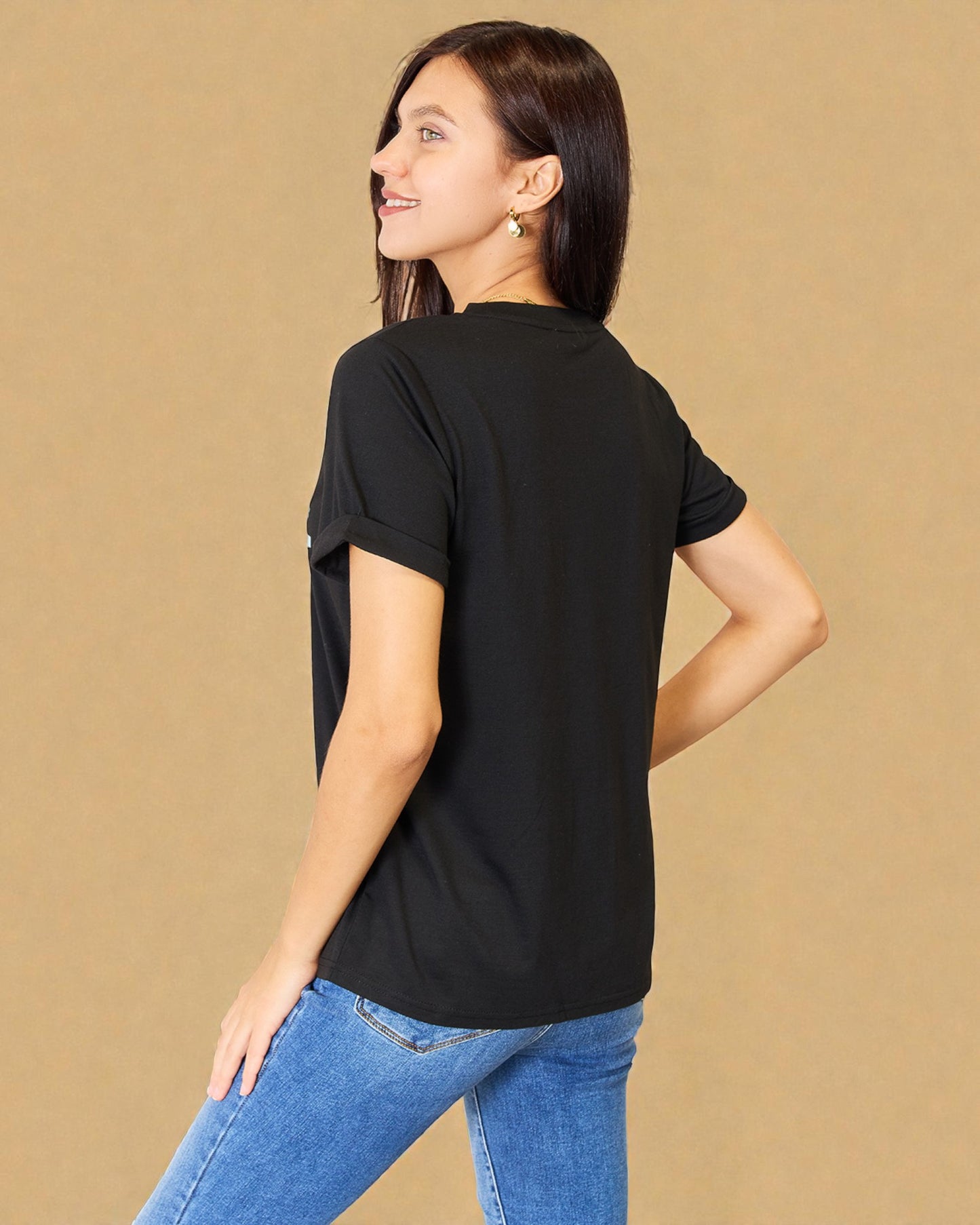 Woman wearing a black t-shirt and blue jeans against a beige background