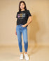 Woman wearing a black t-shirt with colorful text and blue jeans on a beige background