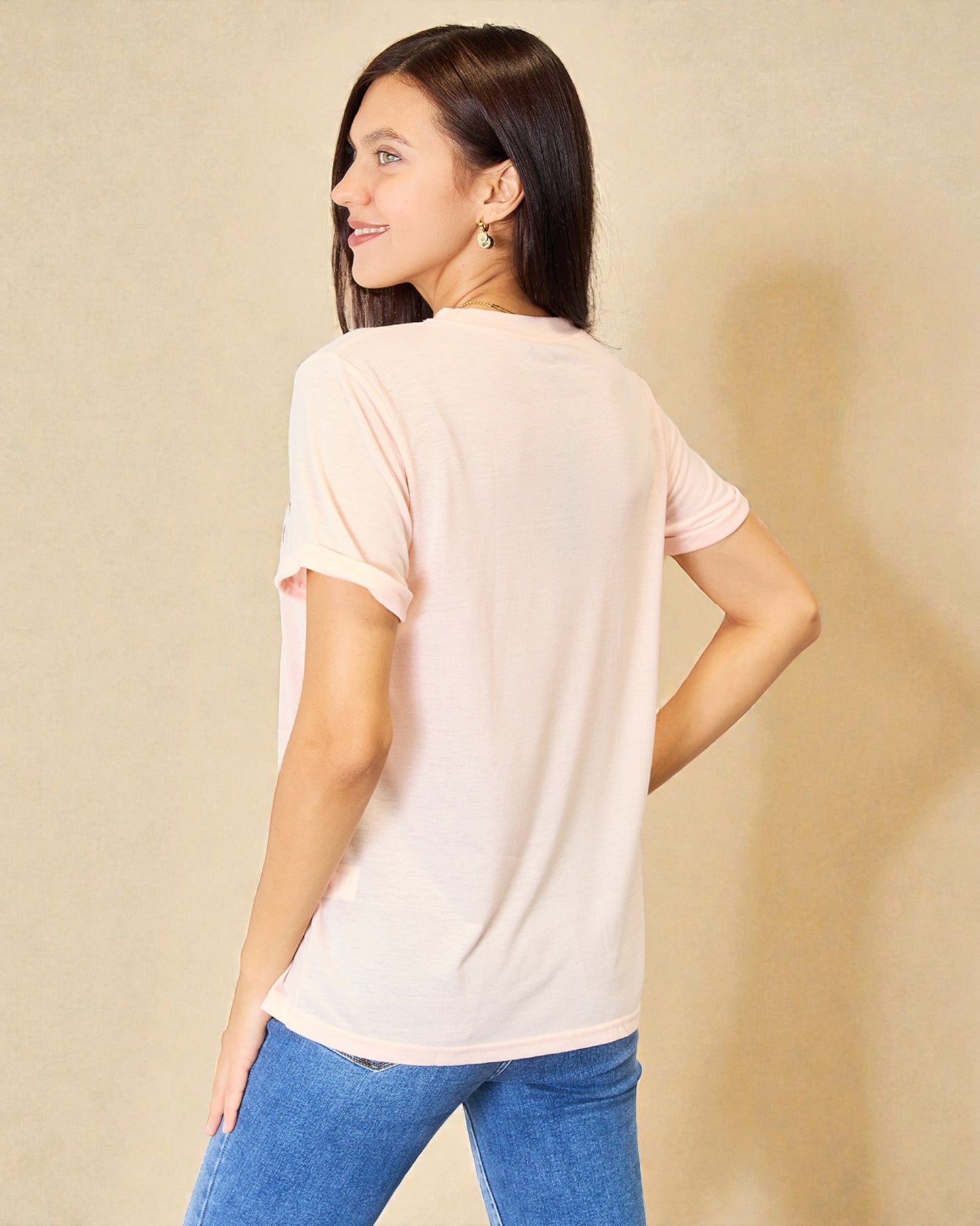 Woman wearing a light pink t-shirt and blue jeans against a beige background