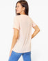 A woman wearing a light peach-pink short-sleeve t-shirt and blue jeans, shown from a back-three-quarter view against a plain white studio background.