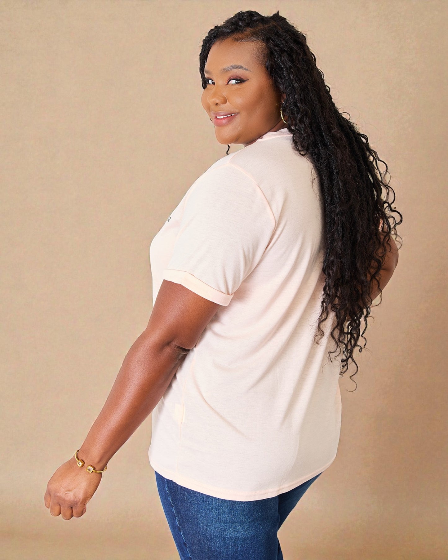Woman wearing a beige shirt and blue jeans against a beige background