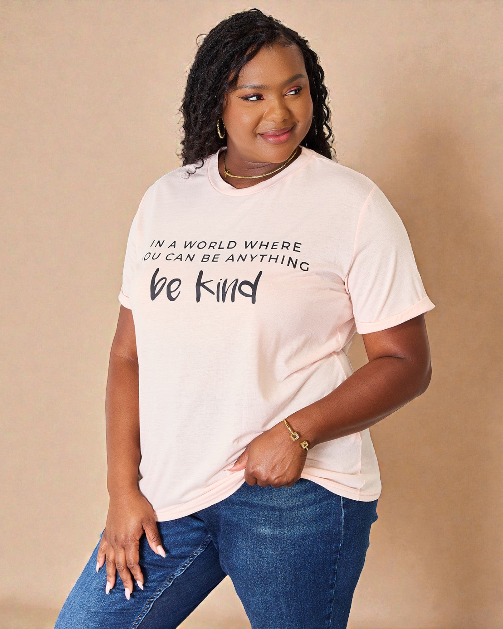 Person wearing a t-shirt with 'In a world where you can be anything, be kind' text on a beige background