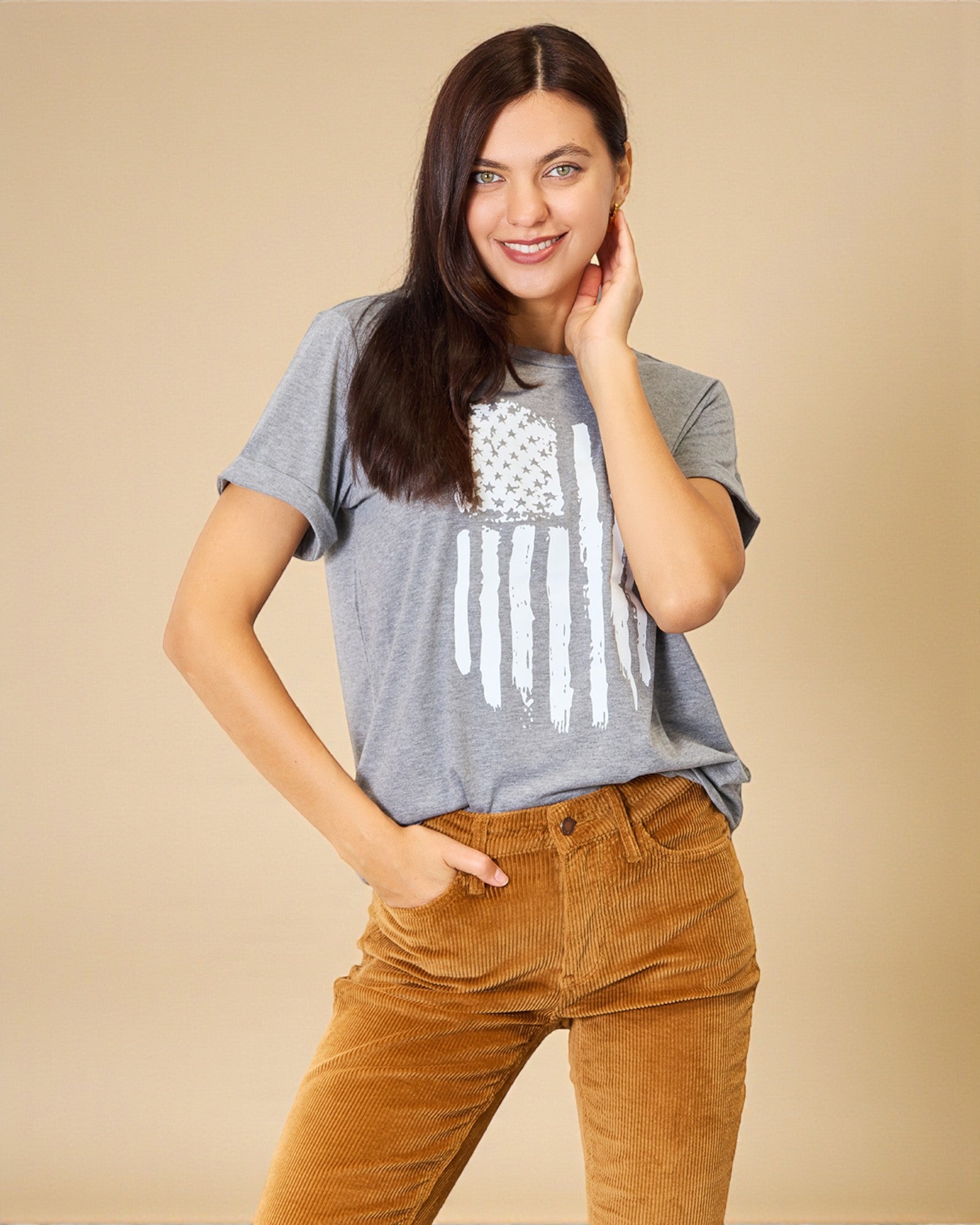 Woman wearing a gray t-shirt with a white graphic design and brown pants on a beige background