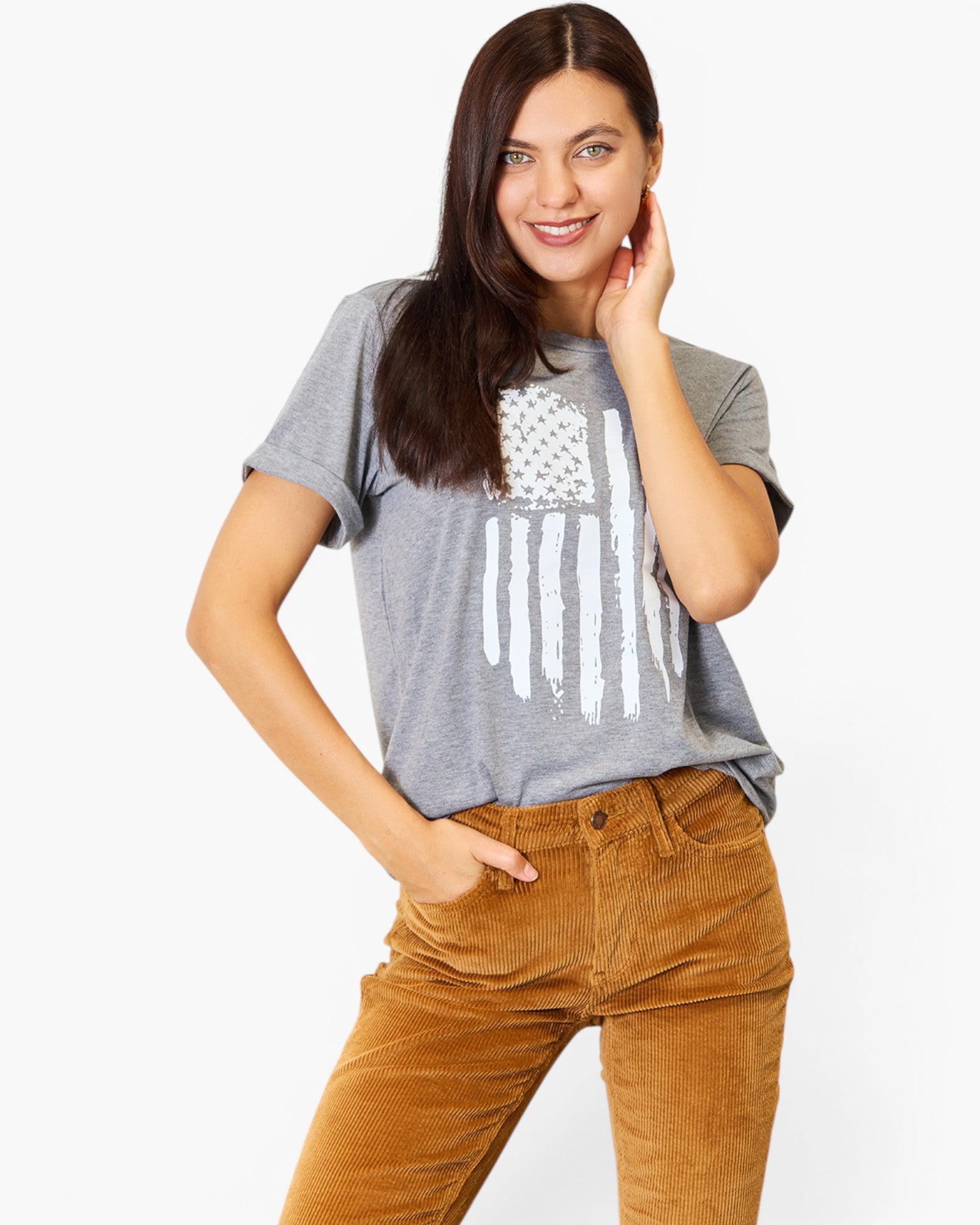 A woman modeling a heather gray t-shirt with a distressed white American flag graphic, paired with brown corduroy pants, against a plain white background.