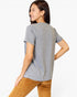 A woman shown from the back wearing a heather gray short-sleeve t-shirt and brown corduroy pants against a plain white studio background.